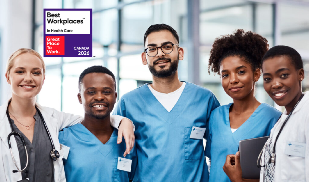 A group portrait of a diverse medical team, including doctors in white lab coats and nurses in blue scrubs, smiling together in a modern clinic or hospital setting. In the top left corner, there is a prominent badge that reads "Best Workplaces in Health Care - Great Place To Work - CANADA 2026".